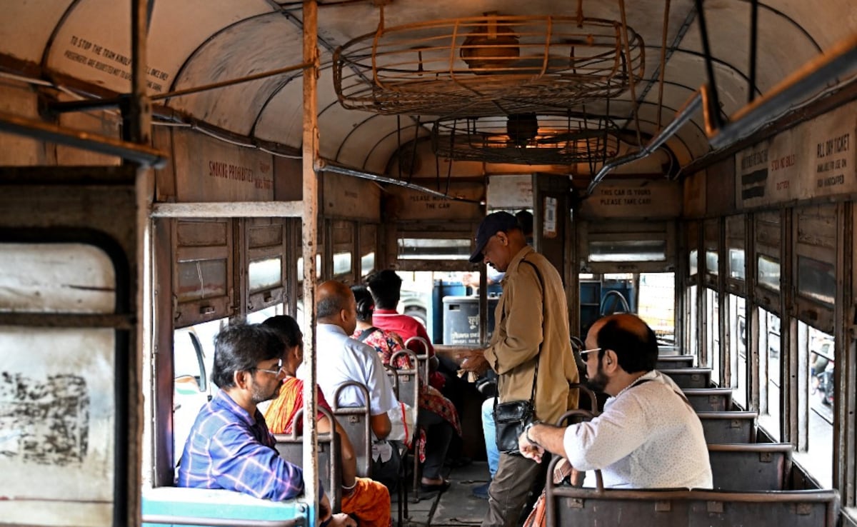 A conductor collects tickets as passengers commute in a tram along a street in Kolkata